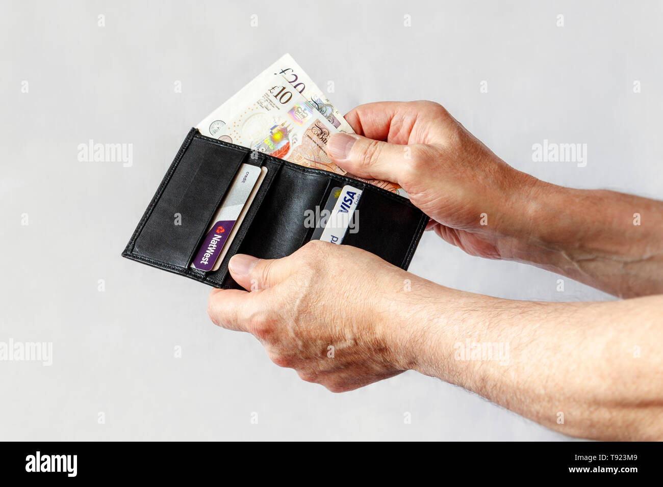 Close-up di un uomo con le mani in mano tenendo una ten-pound e venti-pound nota da un nero portafoglio in pelle, contenente anche le carte di credito Foto Stock