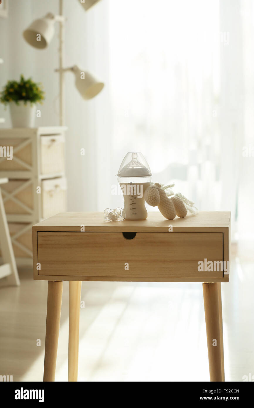 Il biberon con il latte, con il succhietto e il giocattolo sul tavolo in camera di luce Foto Stock