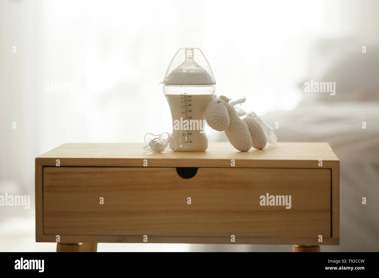 Il biberon con il latte, con il succhietto e il giocattolo sul tavolo in camera di luce Foto Stock