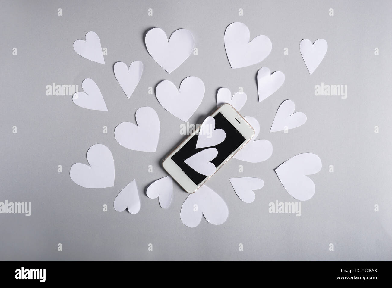Cuori di carta e il telefono cellulare su sfondo grigio Foto Stock