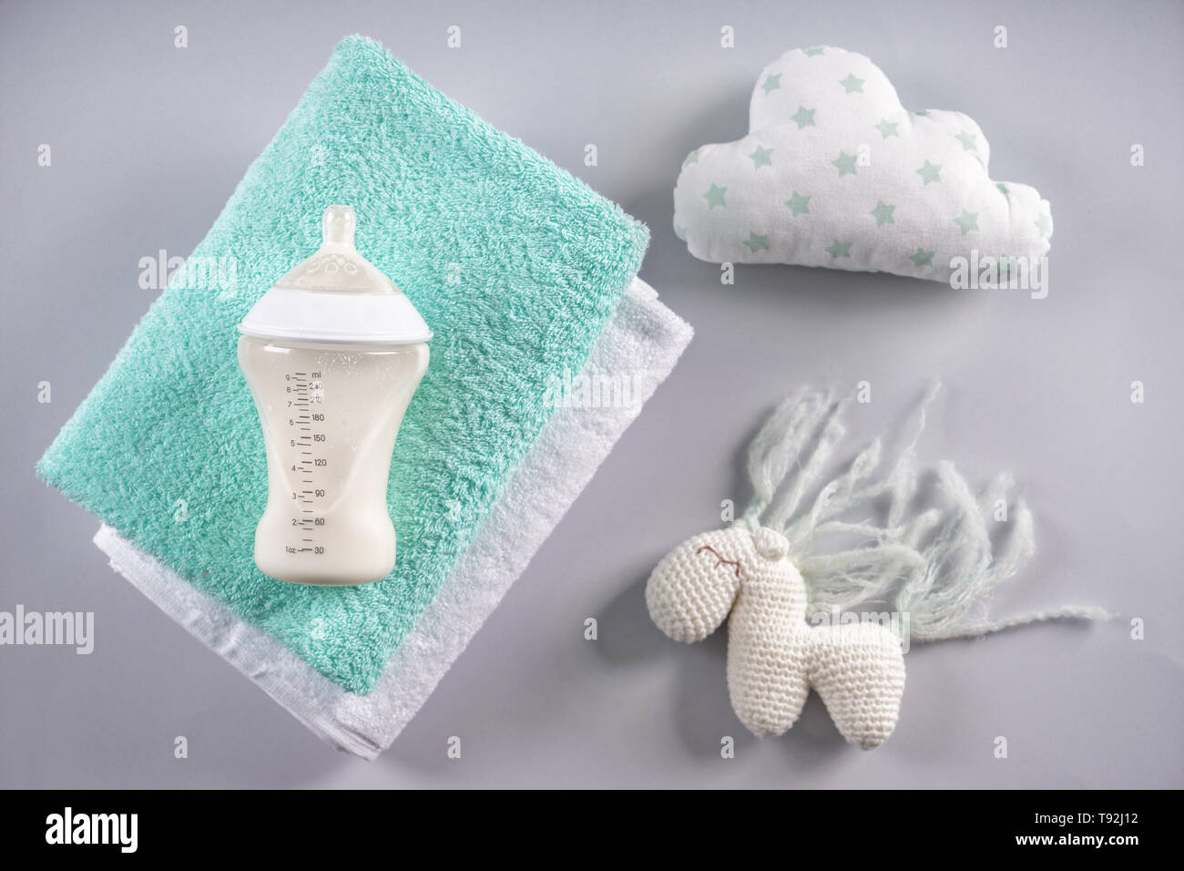 Il biberon di latte per il bambino con asciugamani e giocattoli su sfondo grigio Foto Stock