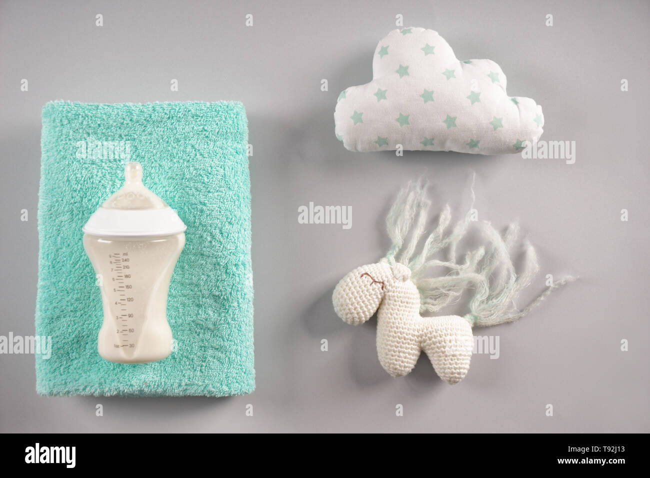 Il biberon di latte per il bambino con un asciugamano e giocattoli su sfondo grigio Foto Stock