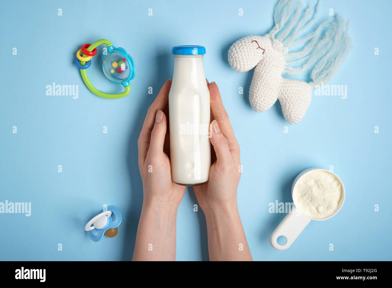Donna che mantiene una bottiglia di latte con polvere e giocattoli sul colore di sfondo Foto Stock