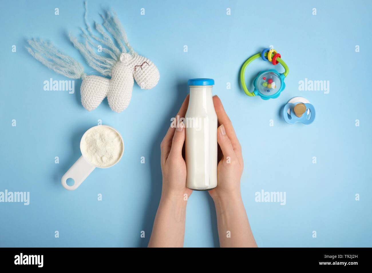 Donna che mantiene una bottiglia di latte con polvere e giocattoli sul colore di sfondo Foto Stock