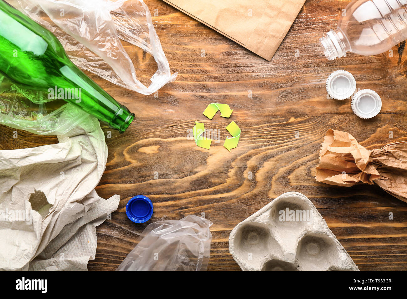 Rifiuti diversi con il simbolo del riciclaggio su sfondo di legno. Concetto di ecologia Foto Stock