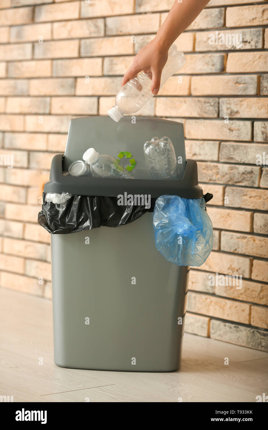 Donna di gettare la bottiglia di plastica nel cestino dell'immondizia vicino a un muro di mattoni Foto Stock