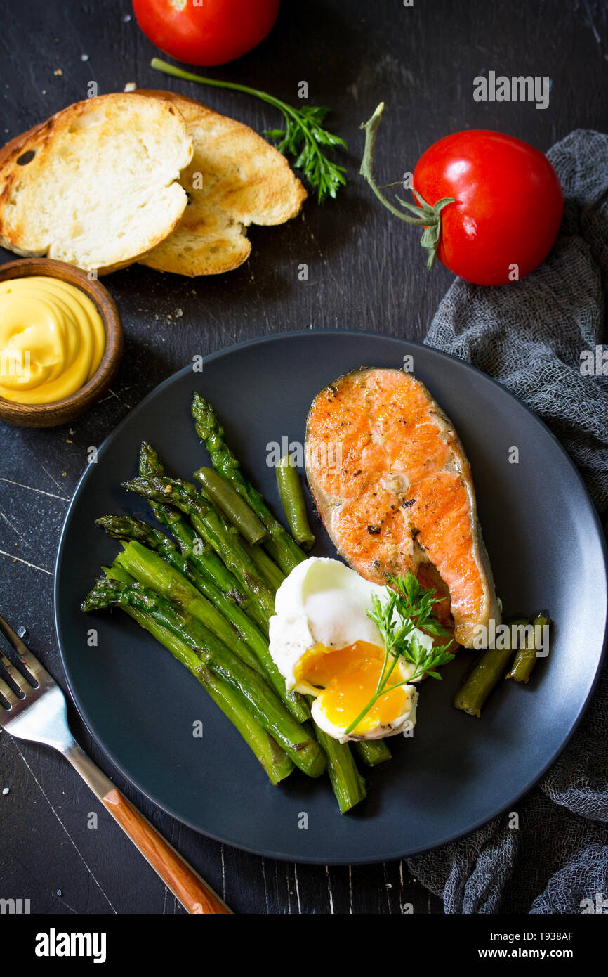 Pesce salmone bistecca alla griglia con asparagi, Uovo affogato su sfondo nero. Cibo sano. Foto Stock