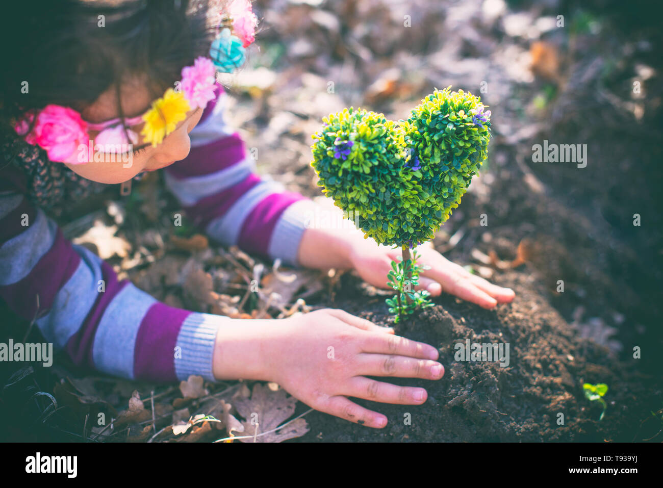 Bellissima bambina di piantare un a forma di cuore ad albero e sognare un futuro bello Foto Stock