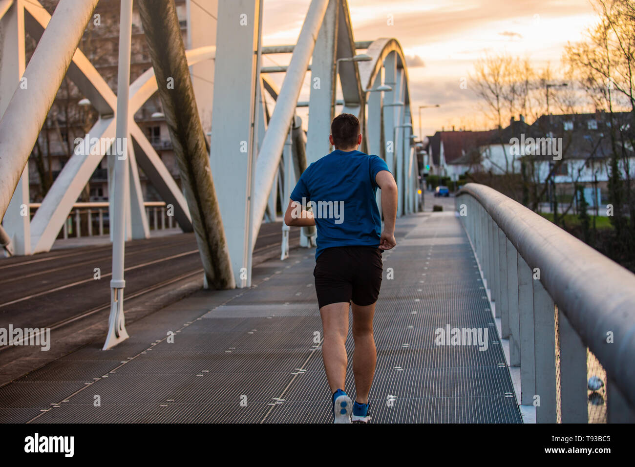 Atletica Giovane uomo praticando sport all'aperto, corre veloce lungo il ponte sopra il Cielo di tramonto sullo sfondo. Auto conquistando superare ostacoli e vincere. Egli Foto Stock