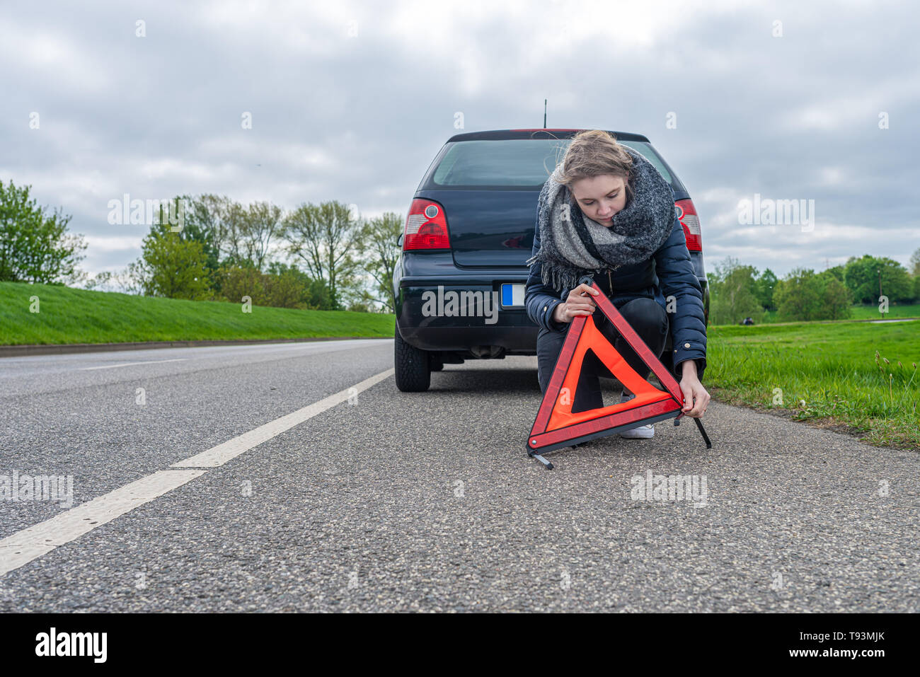 Una giovane donna assembla un triangolo di avvertenza nella parte anteriore della sua automobile Foto Stock
