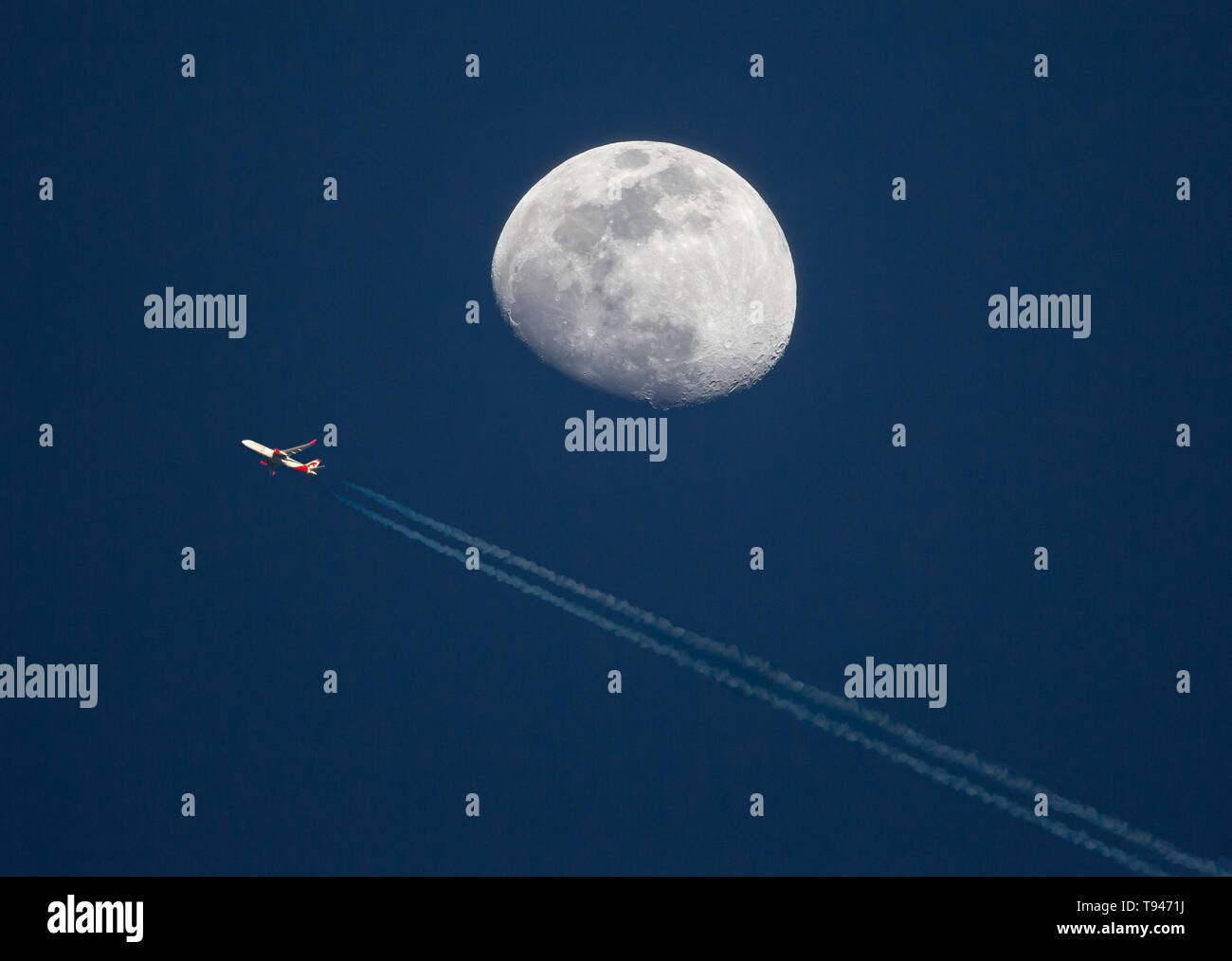 Un aereo commerciale ad alta altitudine passa vicino a waxing gibbous moon al tramonto. Foto Stock