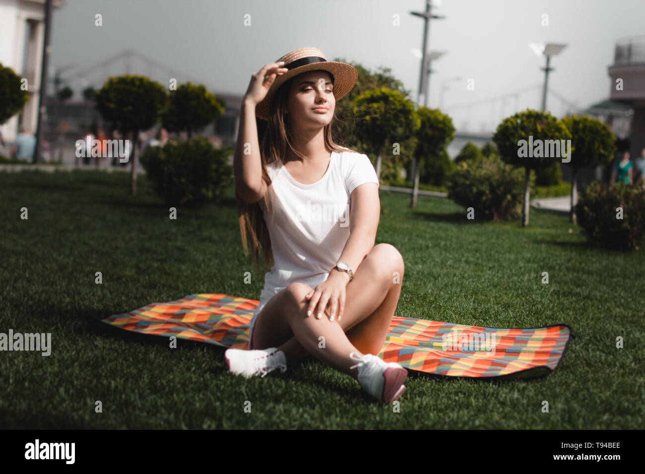 È una ragazza seduta sulla coperta sull'erba nel parco con gambe incrociate. Foto Stock