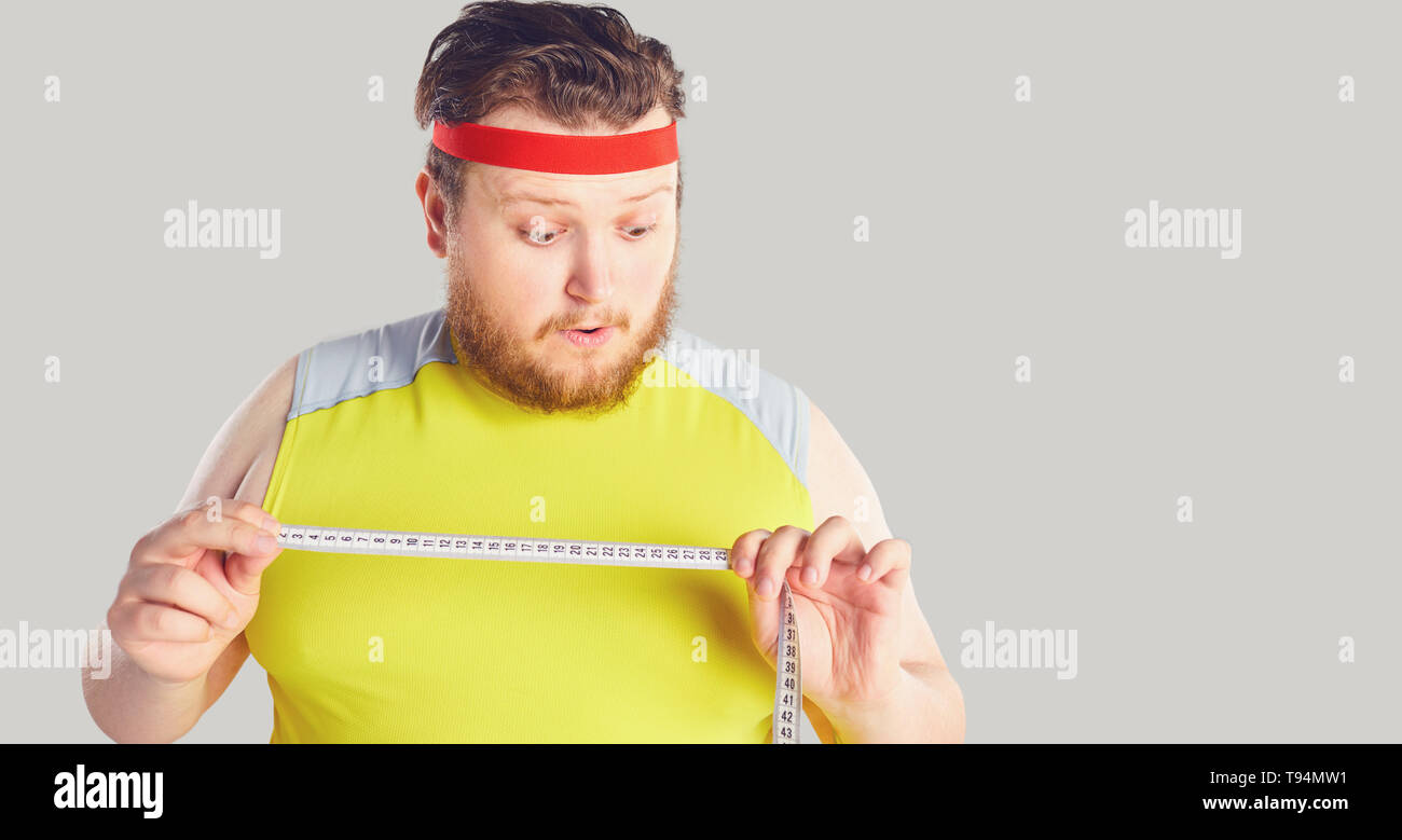 Funny uomo grasso con la barba tenendo un centimetro nelle sue mani con la divertente emozione. Foto Stock