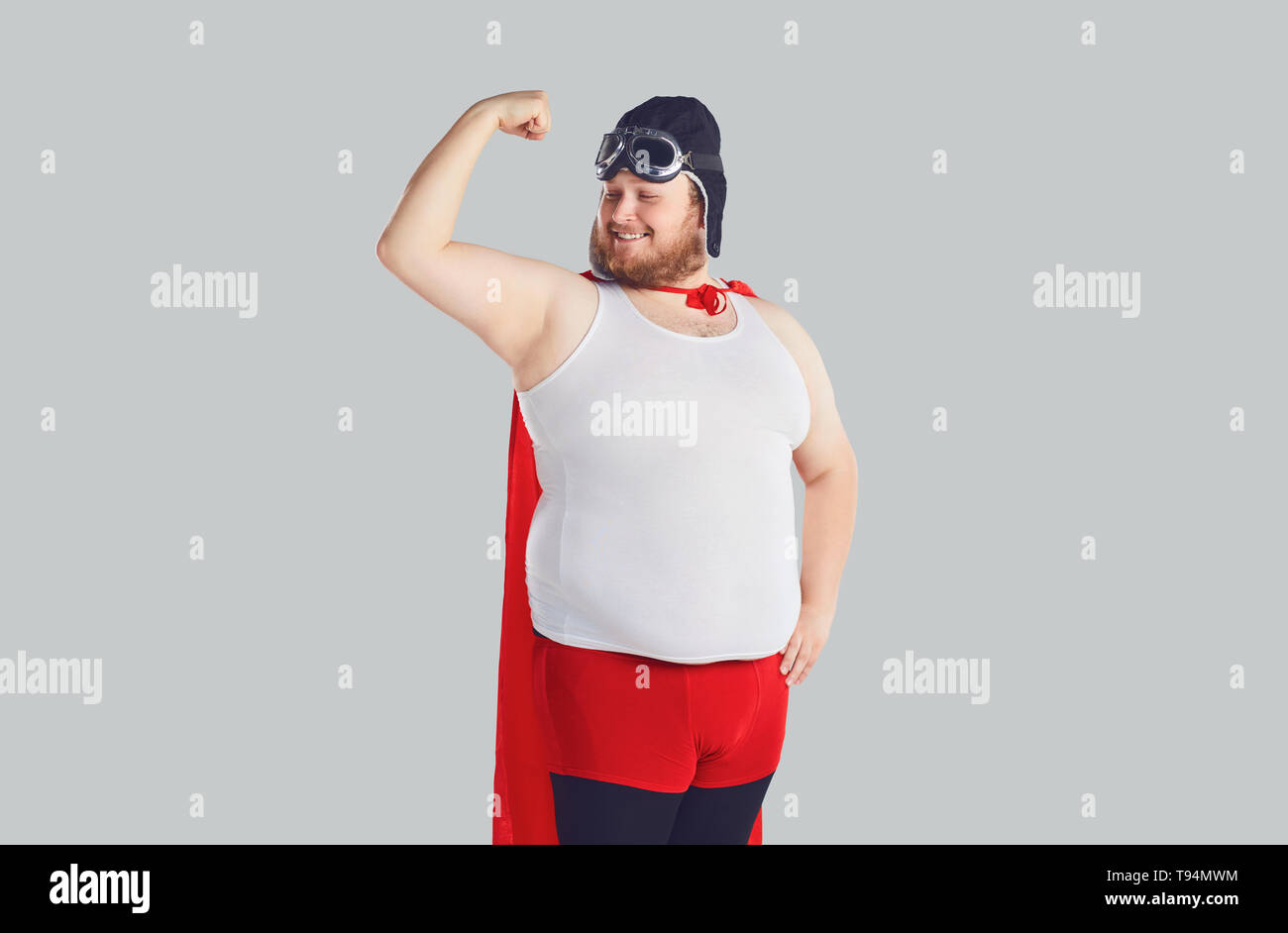 Funny uomo grasso in un costume da supereroe ha sollevato la sua mano. Foto Stock