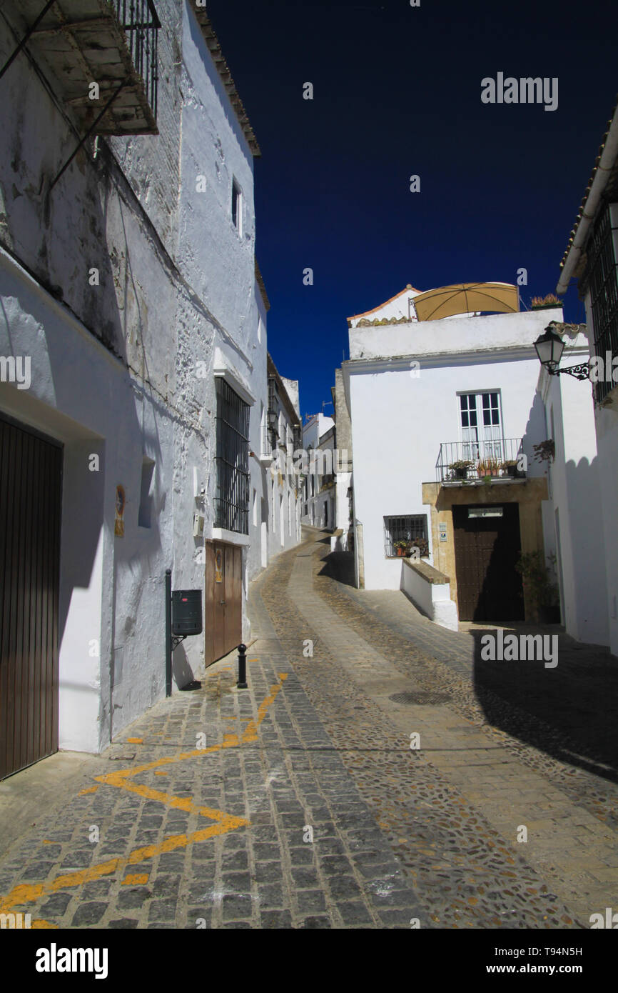 Luminoso e brillante vuoto isoalated stretto vicolo con ciottoli contro il profondo blu del cielo e tipico spagnolo case bianco - Arcos de la Frontera, Andalusia Foto Stock