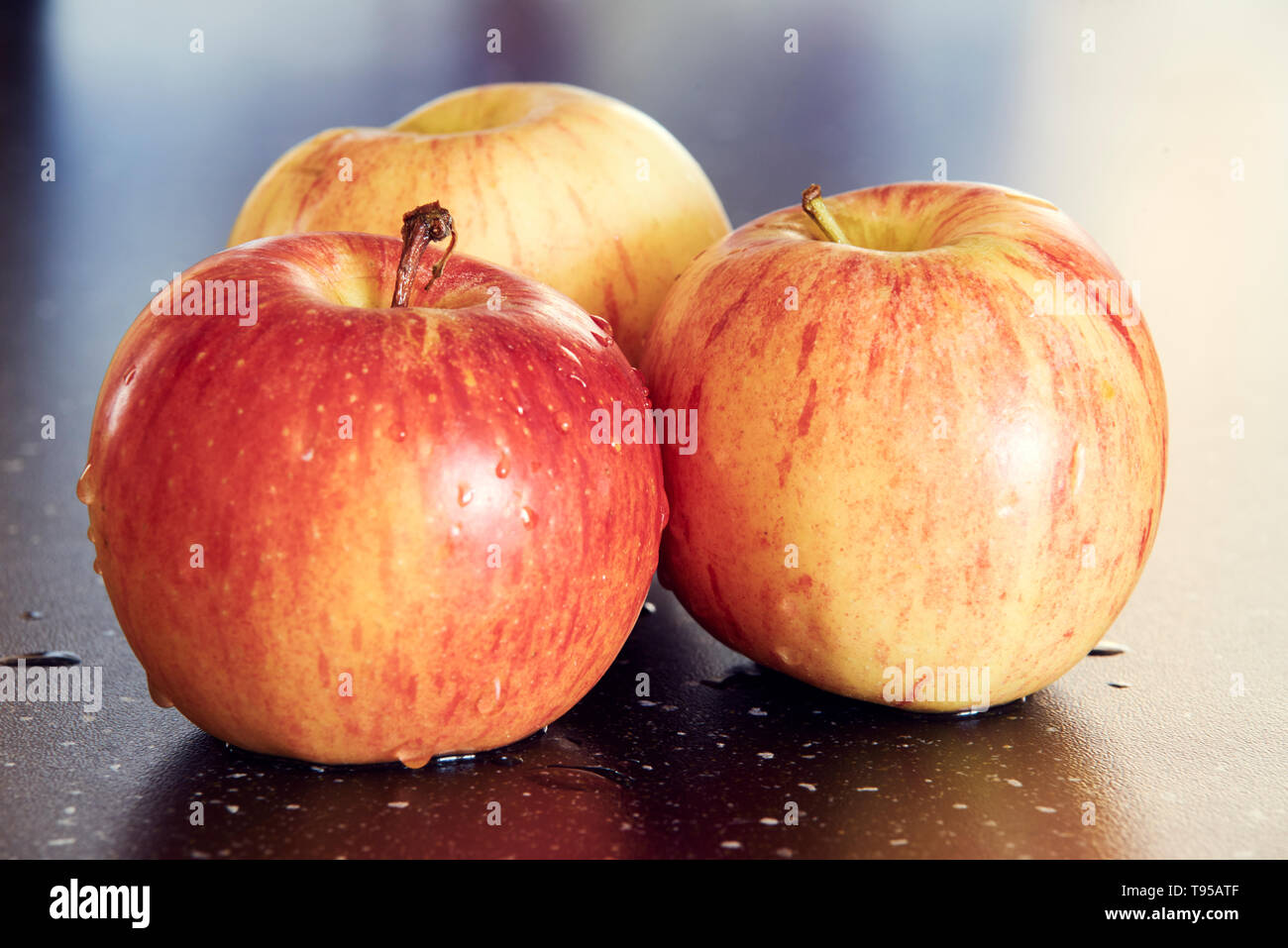 Macrofotografia dettagliata di colore giallo-tre mele rosse su scuro lucido tavolo. Dolce e mele fresche con gocce d'acqua sulla tabella scuro con awesome bokeh di fondo. Foto Stock