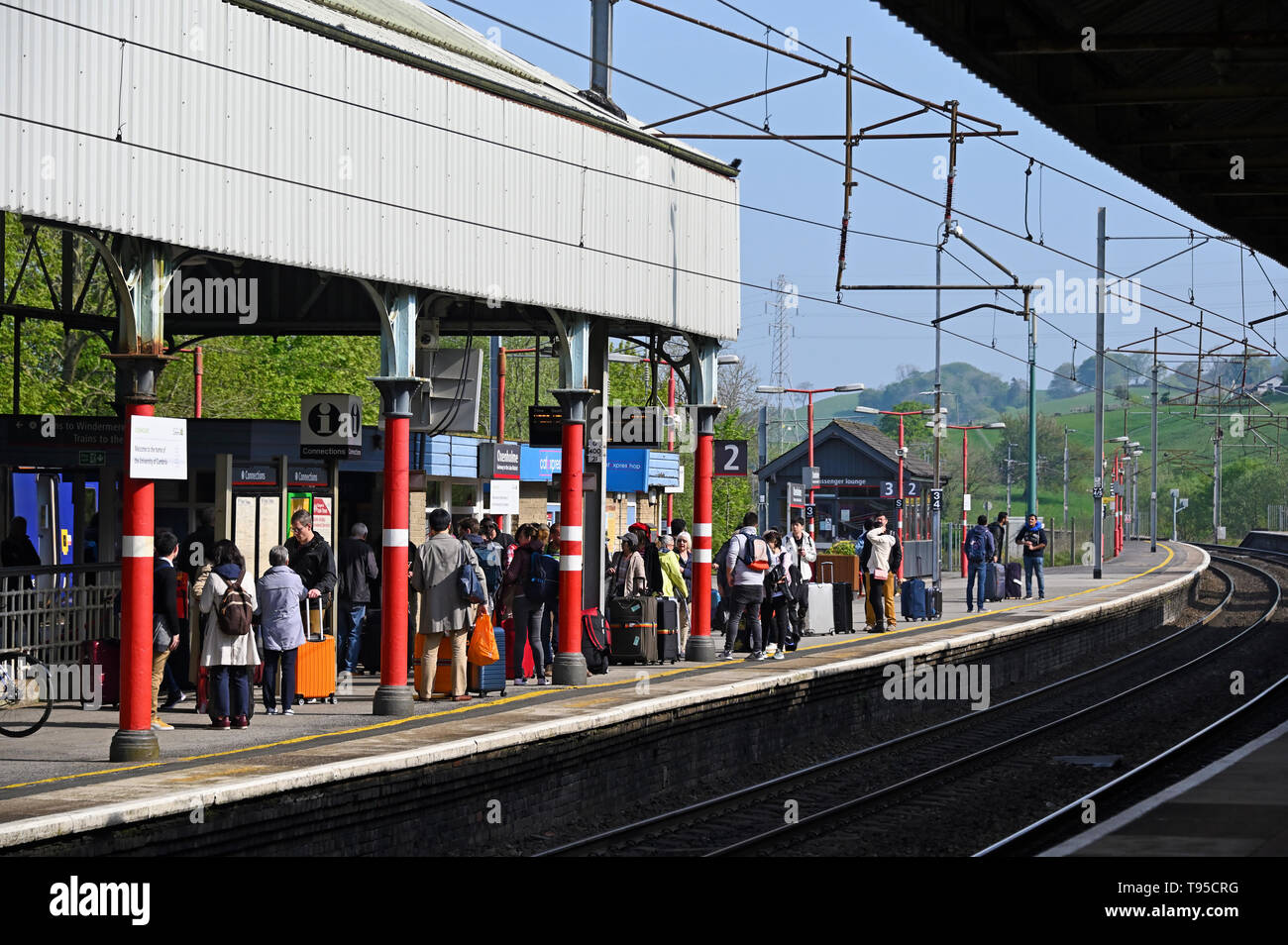 I passeggeri in attesa di un treno sulla piattaforma verso nord fino alla stazione di Oxenholme, Linea principale della costa occidentale, Cumbria, England, Regno Unito, Europa. Foto Stock