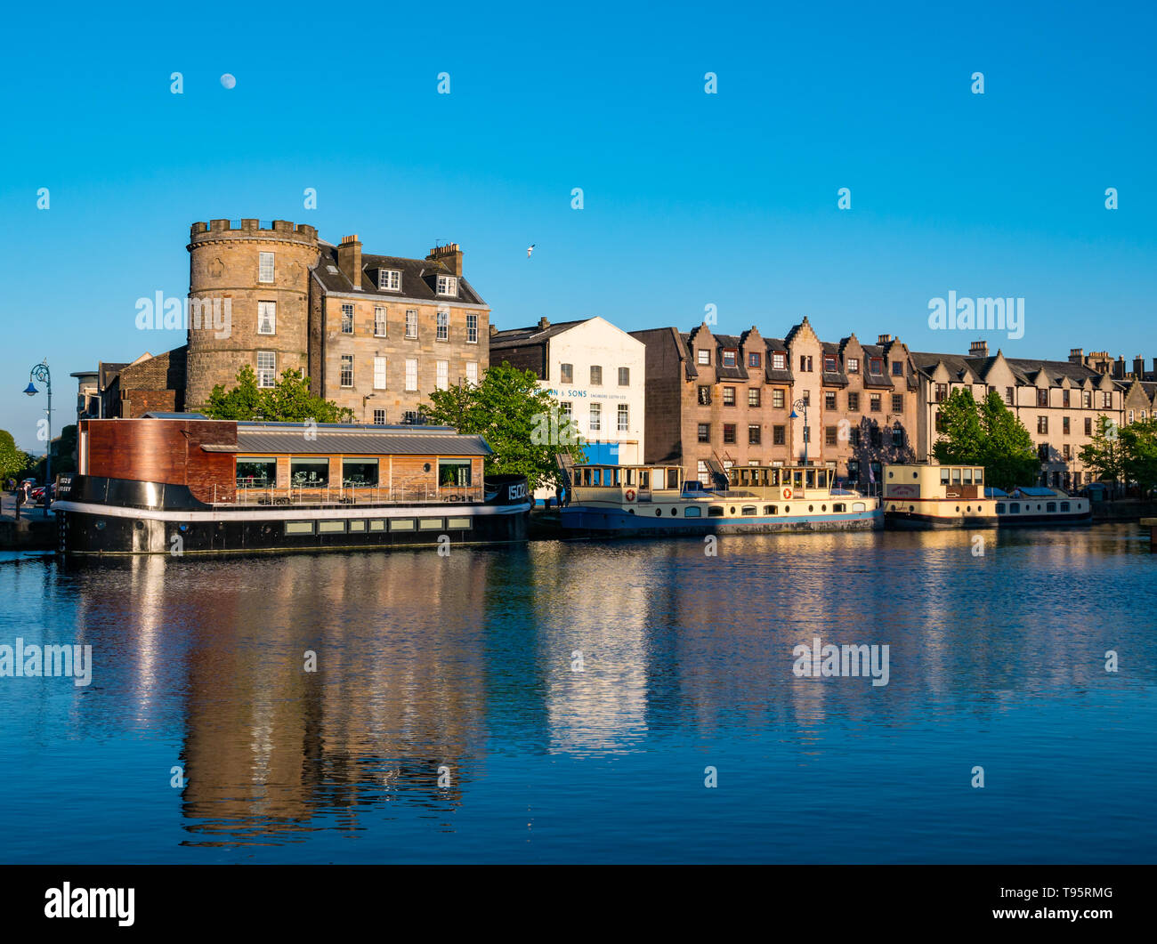 Leith Docks, Edimburgo, Scozia, Regno Unito, 16 maggio 2019. Regno Unito Meteo: una giornata di sole arriva alla fine sopra l'area del porto in Leith con edifici e chiatte sulla riva illuminato dagli ultimi raggi del sole riflessi nell'acqua del fiume di Leith Foto Stock