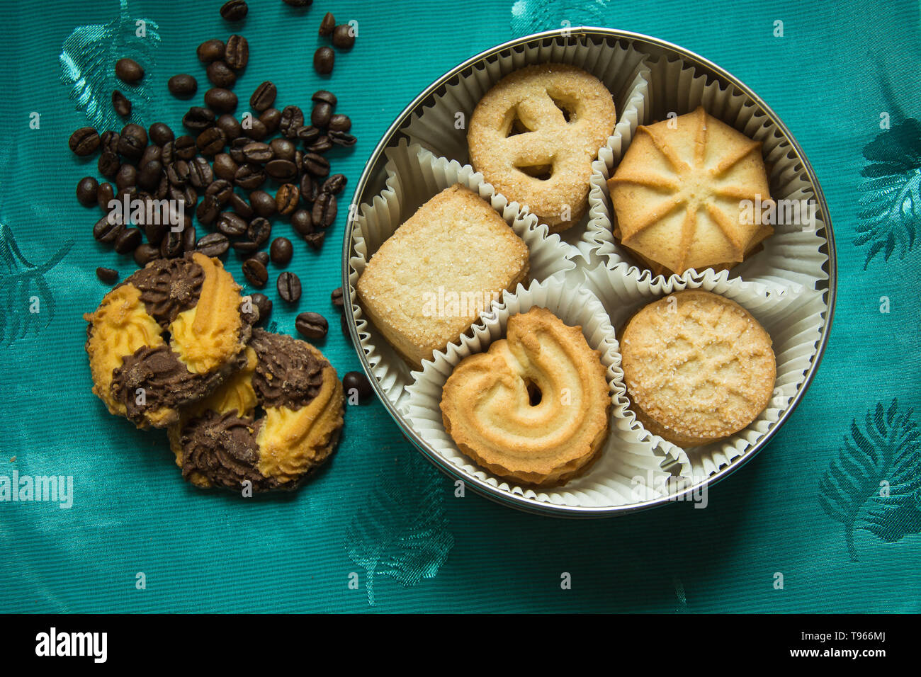 I biscotti con lo zucchero in una scatola rotonda e due giacciono su una tovaglia verde con i chicchi di caffè Foto Stock