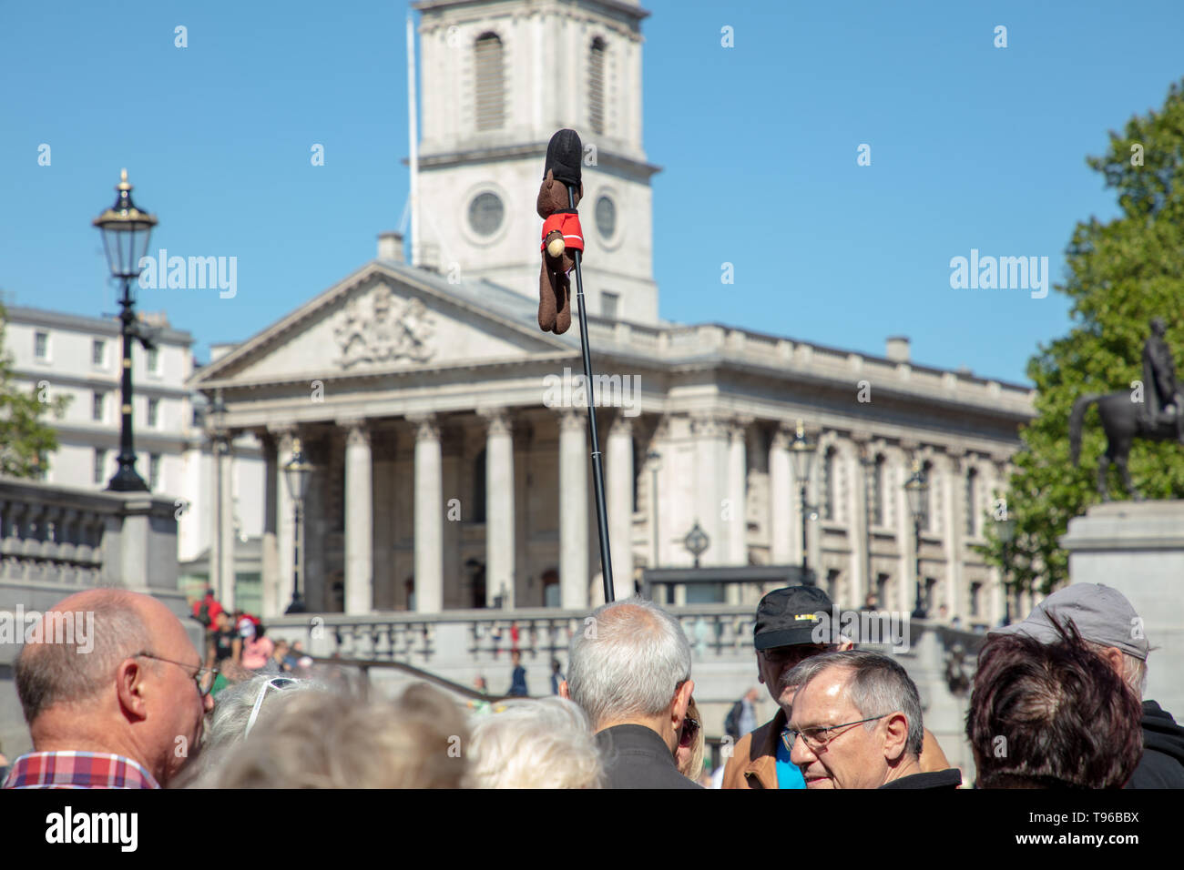 La guida turistica di pensionati leader su un tour a piedi attorno a Trafalgar Square con un lungo bastone e una piccola figura attaccato su un giorno caldo e soleggiato in primavera. Foto Stock