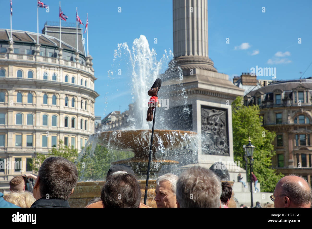 La guida turistica di pensionati leader su un tour a piedi attorno a Trafalgar Square con un lungo bastone e una piccola figura attaccato su un giorno caldo e soleggiato in primavera. Foto Stock