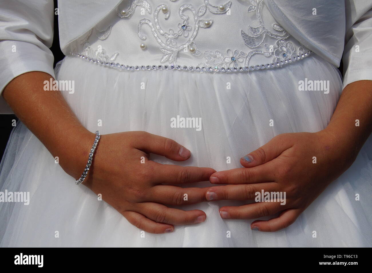 Carino piccolo cild damigella in abito bianco con le mani sul suo ventre. Foto Stock