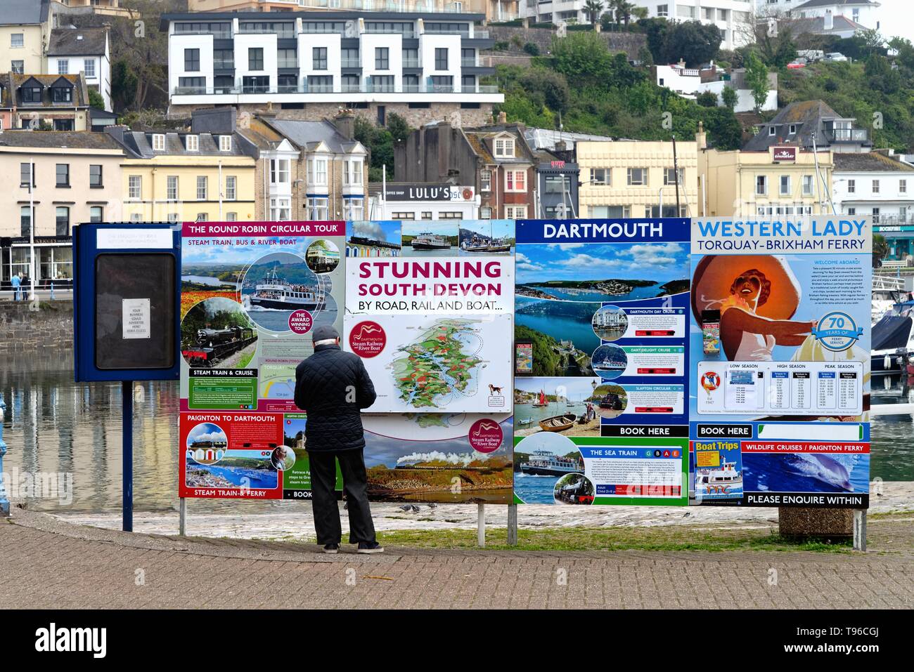 Vista posteriore di un uomo anziano guardando un colorato bacheca in Torquay pubblicità viaggi di turisti su vari tipi di mezzi di trasporto, Devon England Foto Stock