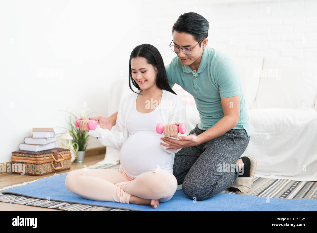 Bella donna incinta facendo esercizio con manubri con mio marito aiutare sua moglie a casa sano concetto Foto Stock