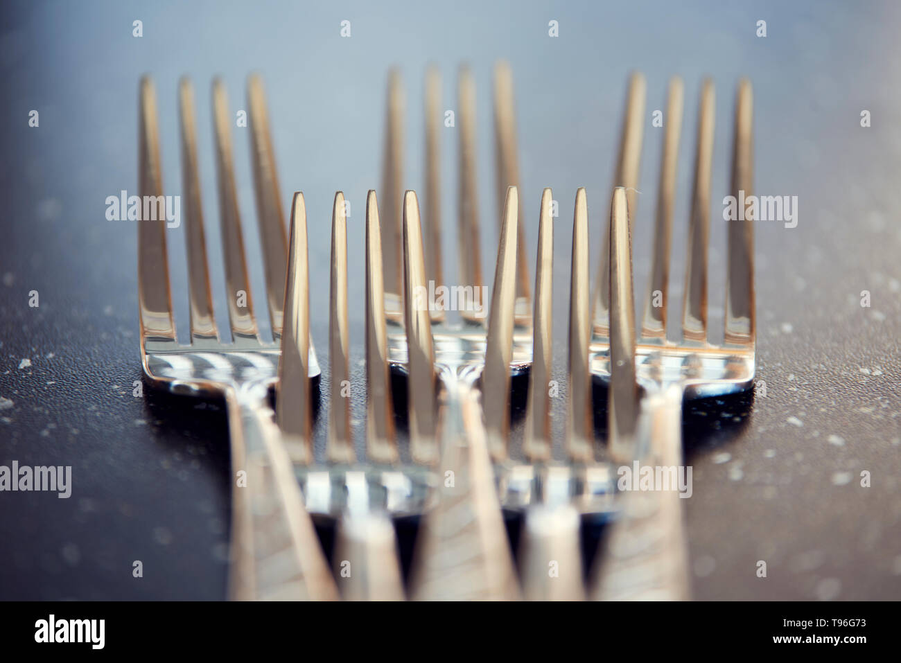 Cinque forcelle in acciaio nero sul tavolo lucido. La fotografia macro per stoviglie design e cucina tema. Foto Stock