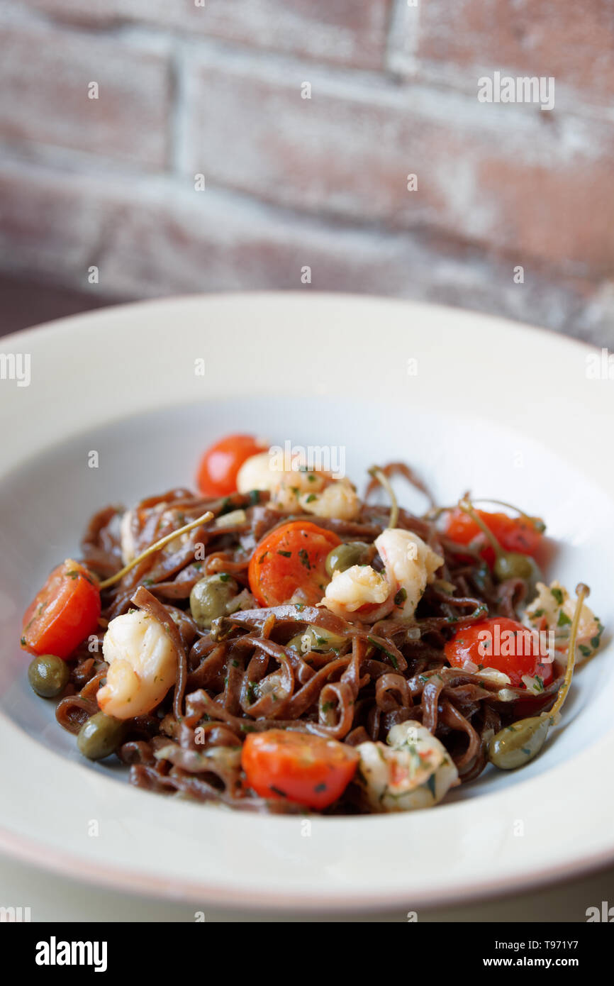 Segale pasta con capperi e gamberi in bianco la piastra di porcellana, close-up Foto Stock