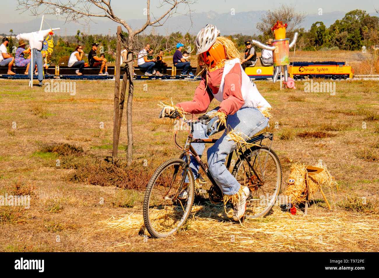 Un Halloween spaventapasseri su una bicicletta con un cane di paglia è giustapposto con altri scarecrows come una gita in treno in miniatura soffi in passato una Costa Mesa, CA, parco. Foto Stock