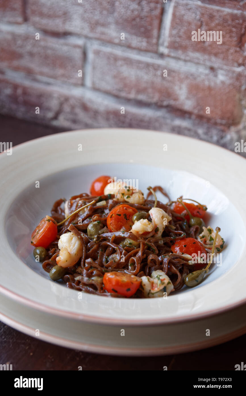 Segale pasta con capperi e gamberi in porcellana bianca piastra contro un muro di mattoni Foto Stock