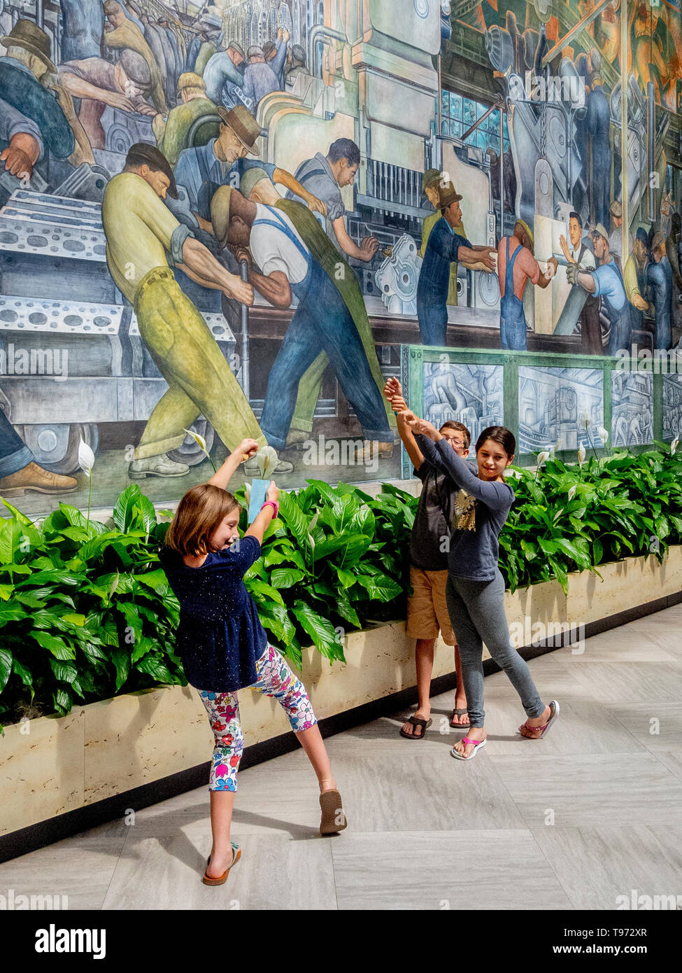 Mentre un amico prende una foto, bambini imitare le pose del settore auto operai ritratte in Diego Rivera il famoso Ford Motor Company affreschi al Detroit Institute of Art. Foto Stock