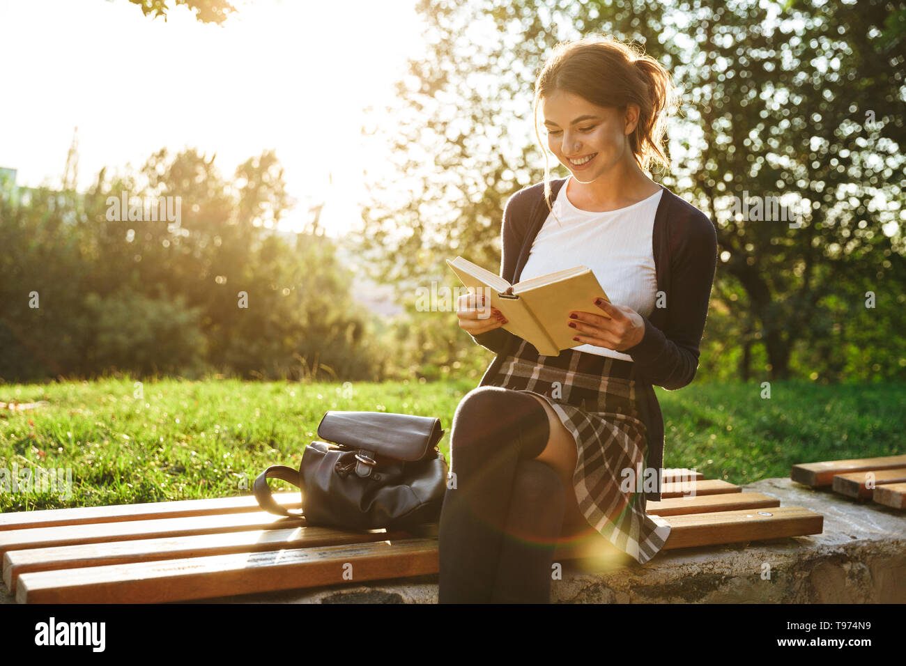 Bella ragazza adolescente indossano uniformi scolastiche libro lettura mentre è seduto su una panchina nel parco Foto Stock