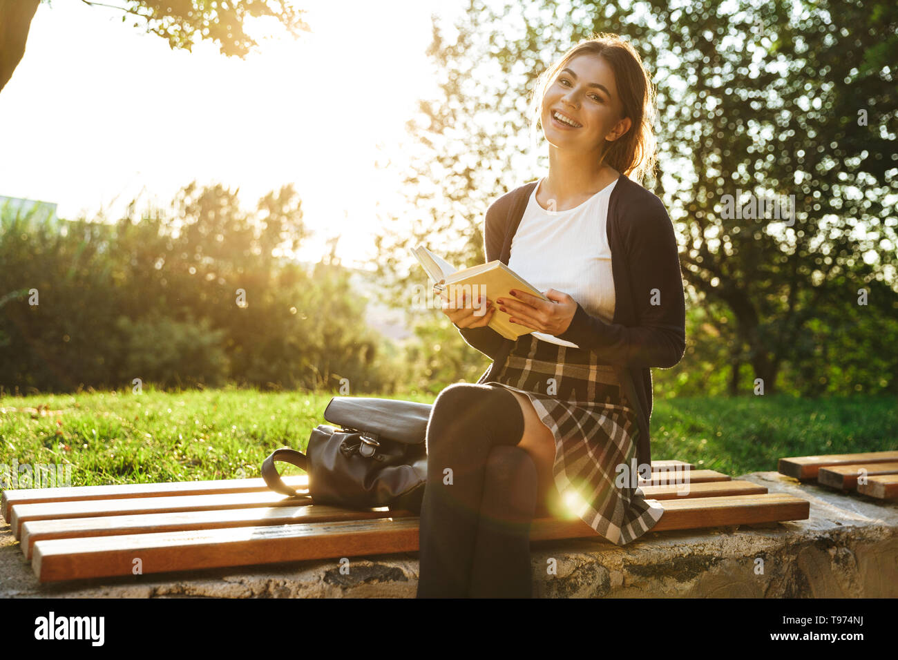 Bella ragazza adolescente indossano uniformi scolastiche libro lettura mentre è seduto su una panchina nel parco Foto Stock