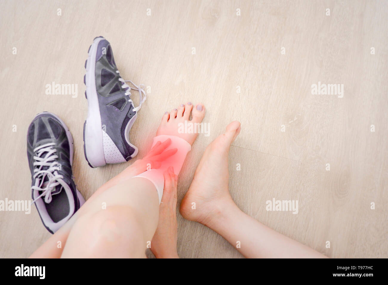 Donna piede con garza bendaggio elastico e scarpe viola (Sneakers). Mani sulle lesioni sportive con macchia rossa. Irriconoscibile feriti piedi sulla seduta del dolore. Foto Stock