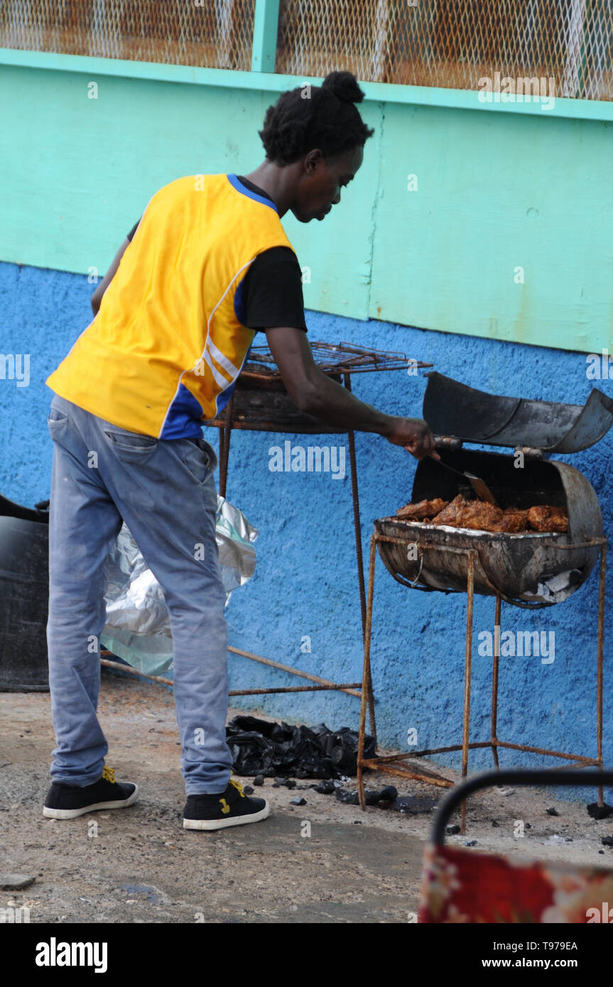 Port Antonio, Portland, Giamaica - 18 Giugno 2017 : un uomo giamaicano di cottura è il ben noto pollo jerk su un vecchio arrugginito grill vicino a Port Antonio in marmellata Foto Stock