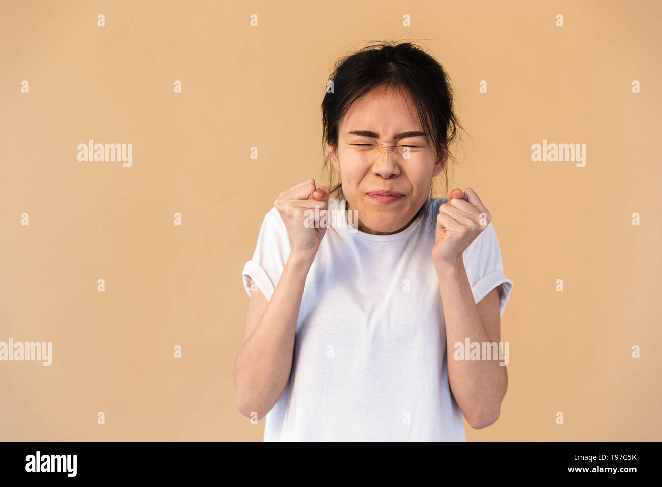 Foto di successo della korean donna che indossa base t-shirt sorridente e stringendo i pugni isolate su sfondo beige in studio Foto Stock