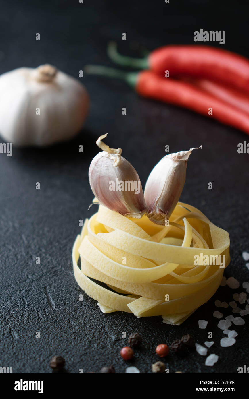 Su uno sfondo nero materie fettuccine hanno due spicchi di aglio, cosparso con sale marino, una miscela di peperoni, peperoncino e una intera testa di Foto Stock