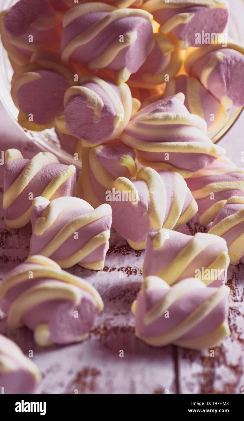 Rosa marshmallows con riccioli di bianco ottenendo abbastanza sonno con un contenitore trasparente sul vecchio di luce sullo sfondo di legno Foto Stock