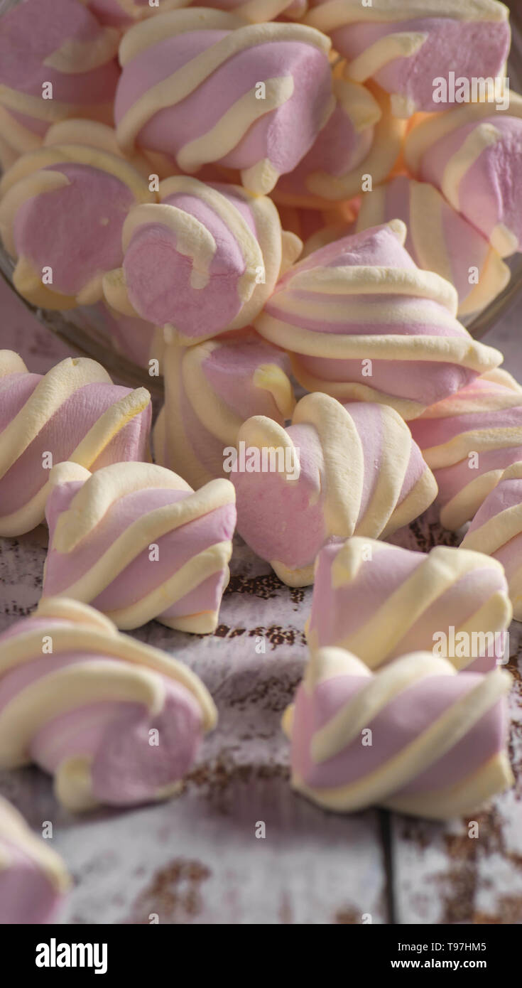 Rosa marshmallows con riccioli di bianco ottenendo abbastanza sonno con un contenitore trasparente sul vecchio di luce sullo sfondo di legno Foto Stock
