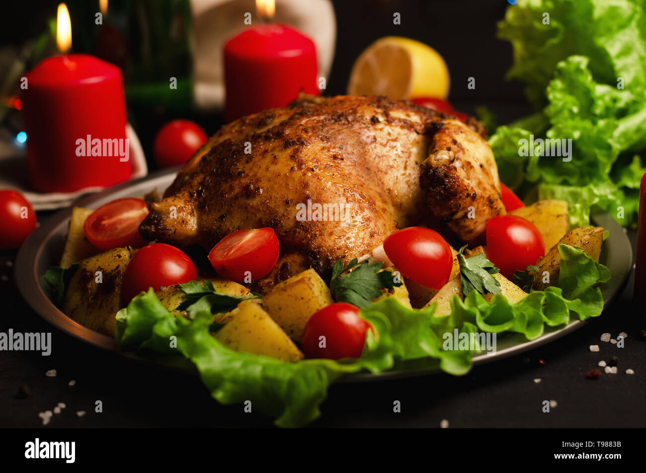 Piatto natalizio. Xmas cotto intero pollo con pomodori e patate close-up su una piastra su un tavolo con candela Foto Stock