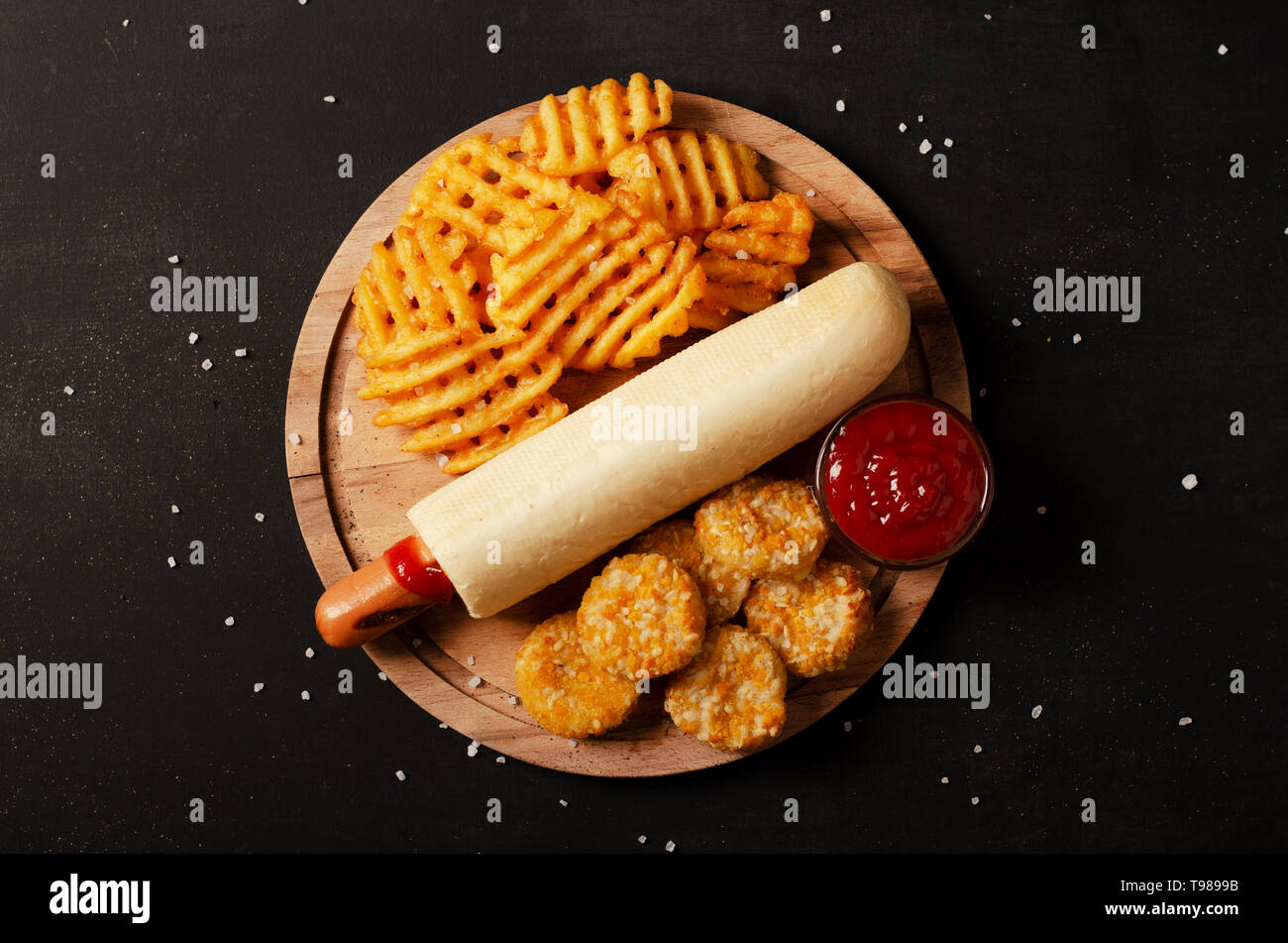 Il francese hot-dog di bun servita con ketchup con croccanti frittelle di patate fritte e pepite di formaggio su uno sfondo nero Foto Stock