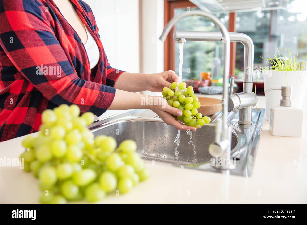 La donna è di risciacquo di uva verde con acqua in cucina e l'uva in primo piano. Foto Stock