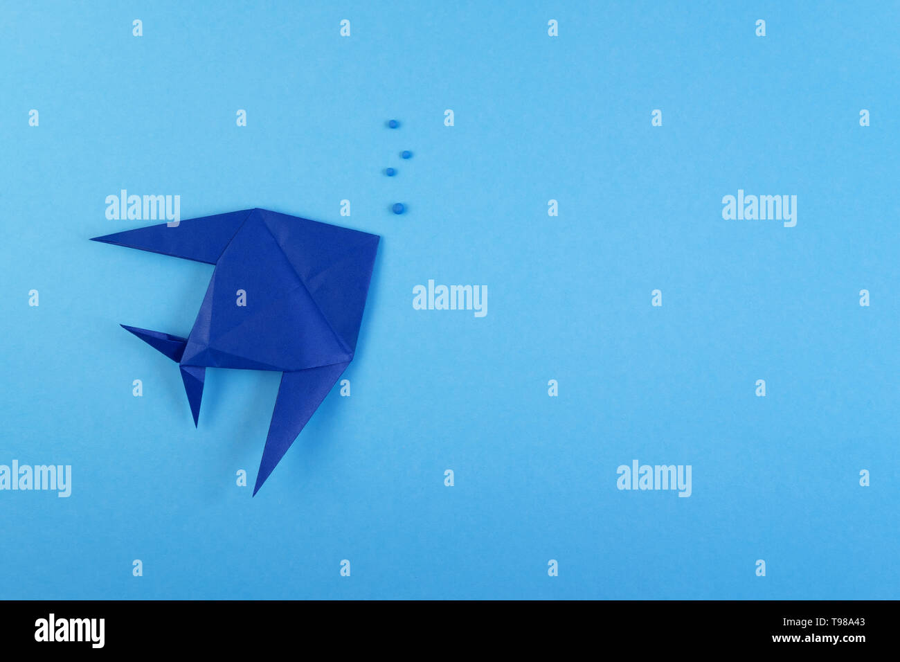Origami pesce tropicale sul cielo azzurro sfondo minimalista. Carta di pesce di mare e bolle sotto l'acqua sullo sfondo del concetto. Hobby, tempo libero, hobby. La vita subacquea, fauna creative lavoro artigianale laici piatta Foto Stock