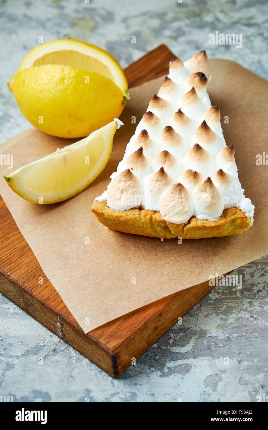 Un pezzo di torta al limone decorata con una fetta di limone su una tavola di legno. Grigio sfondo a trama. Bellissimi piatti di servizio. Il dessert. La catena alimentare Foto Stock