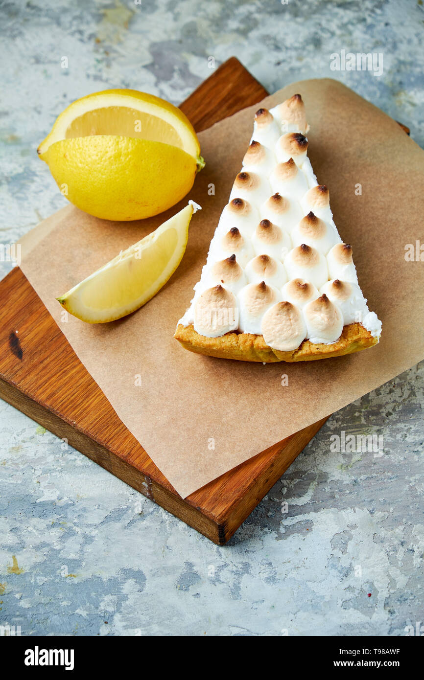 Un pezzo di torta al limone decorata con una fetta di limone su una tavola di legno. Grigio sfondo a trama. Bellissimi piatti di servizio. Il dessert. La catena alimentare Foto Stock