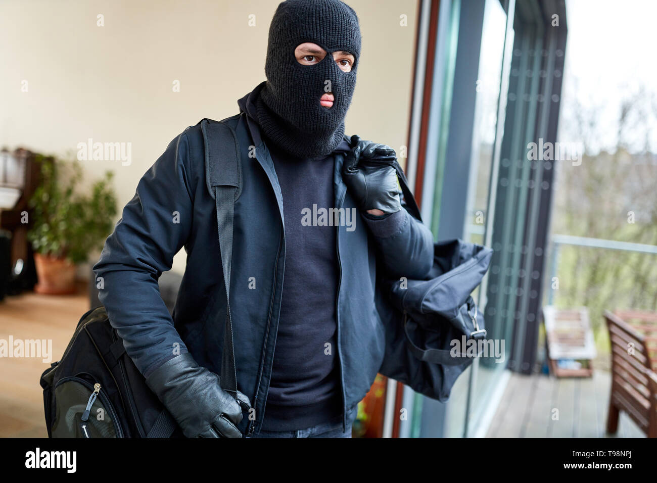 Ladro mascherato fuoriesce da casa con la borsa piena di bottino Foto Stock