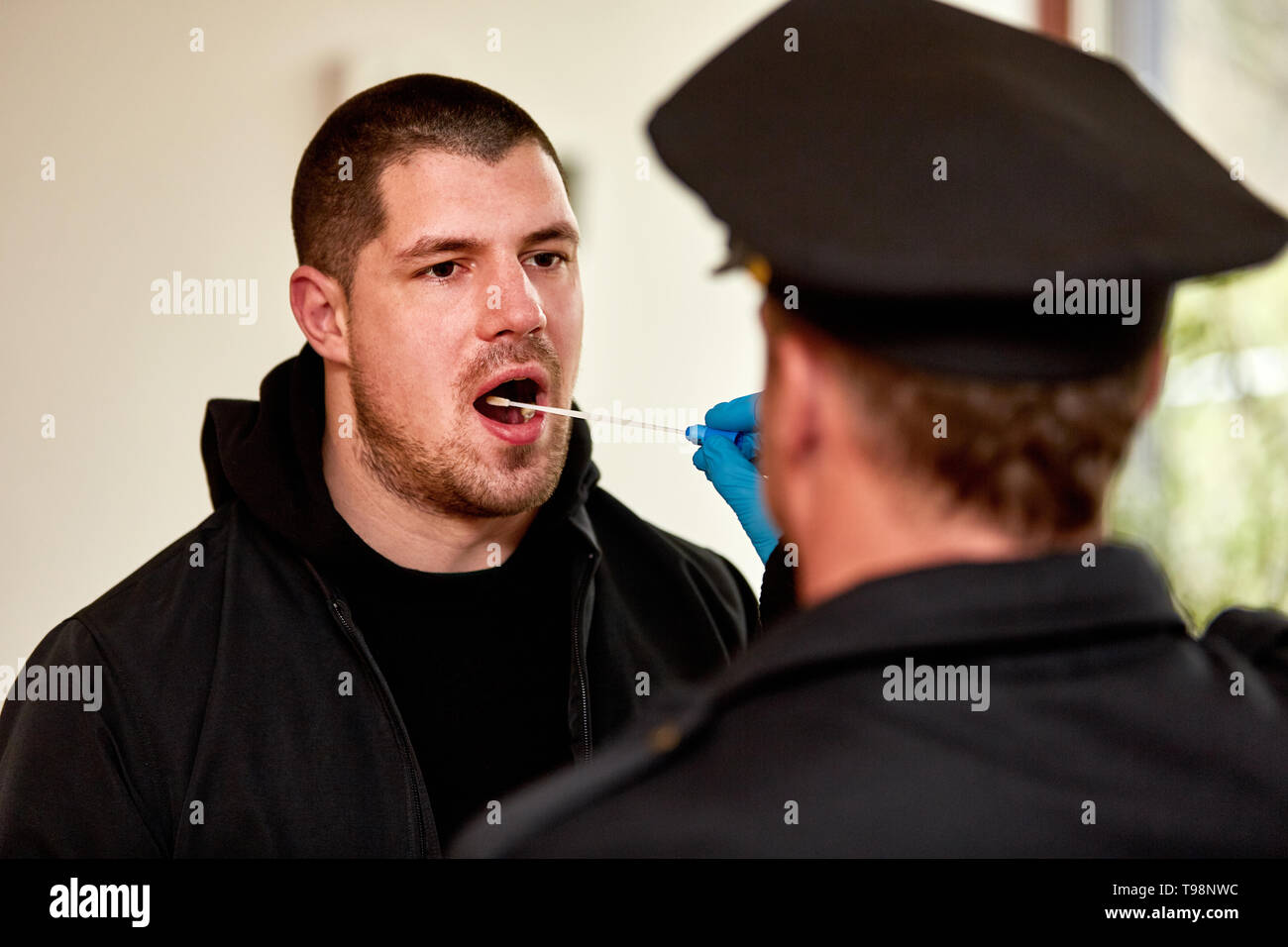Poliziotto tenendo campione di saliva nella cavità orale come un test del DNA Foto Stock