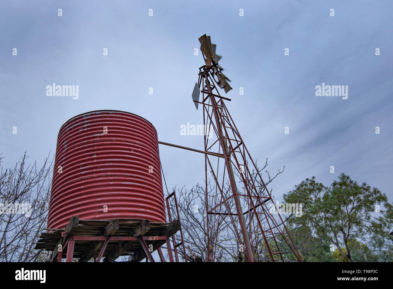 Un vecchio mulino a vento di ferro in una fattoria in western New South Wales, gira nel vento su un giorno nuvoloso con striature di colore grigio sopra le nuvole Foto Stock